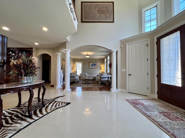 foyer featuring baseboards, ornate columns, recessed lighting, arched walkways, and tile patterned flooring