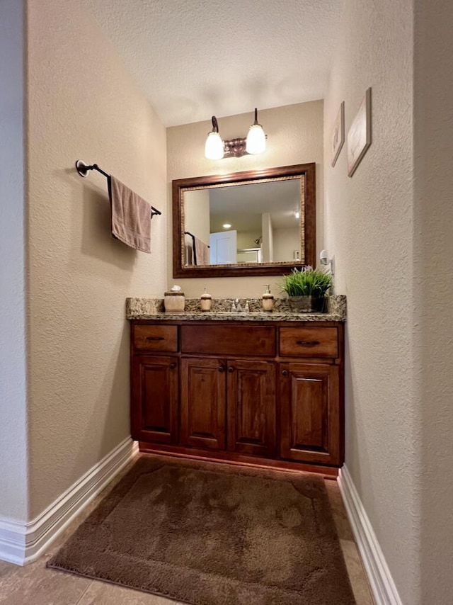 bathroom with baseboards, a textured ceiling, vanity, and a textured wall