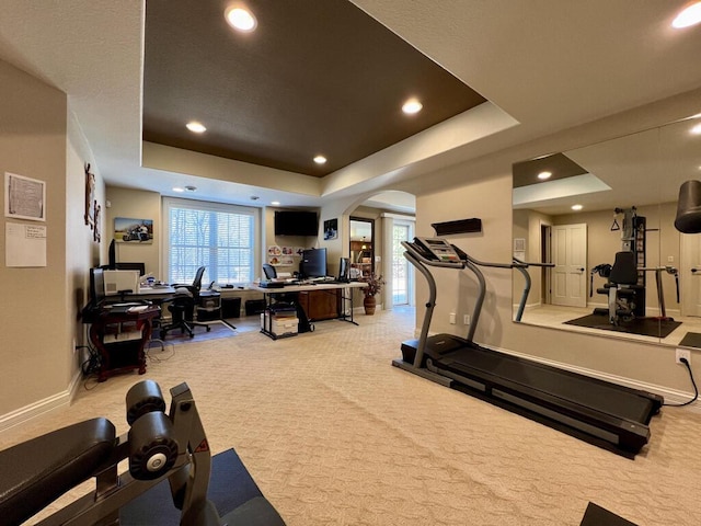 workout area featuring arched walkways, a healthy amount of sunlight, a raised ceiling, and carpet