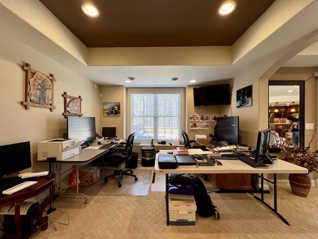 carpeted office space featuring a tray ceiling, recessed lighting, and arched walkways