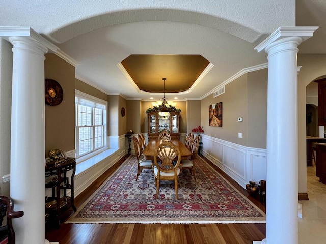 dining room with visible vents, a tray ceiling, arched walkways, wainscoting, and decorative columns