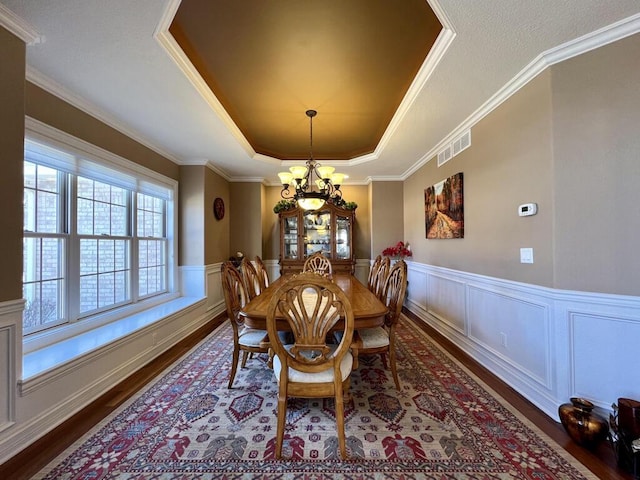 dining space with wood finished floors, a wainscoted wall, visible vents, a tray ceiling, and a chandelier