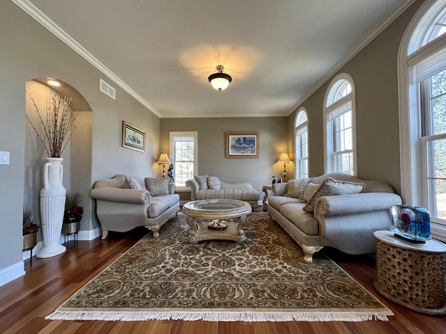 living area featuring visible vents, dark wood-type flooring, ornamental molding, arched walkways, and baseboards