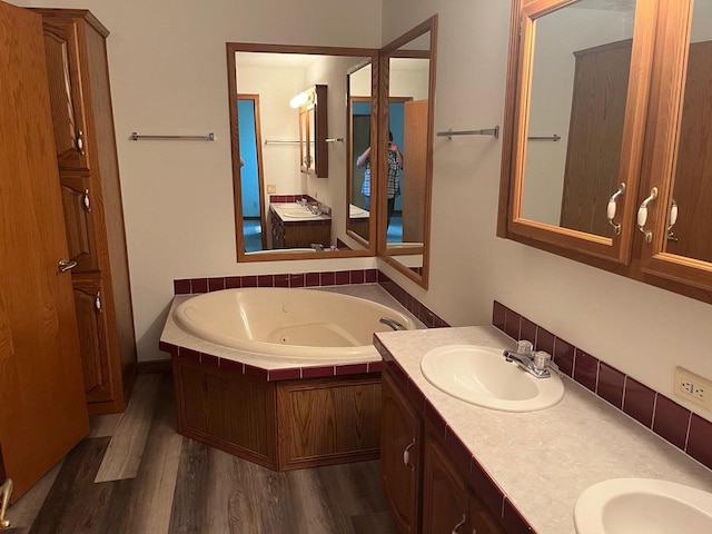 full bath with a sink, a tub with jets, wood finished floors, and double vanity