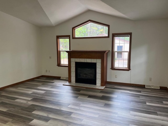 unfurnished living room with visible vents, baseboards, a tiled fireplace, vaulted ceiling, and wood finished floors