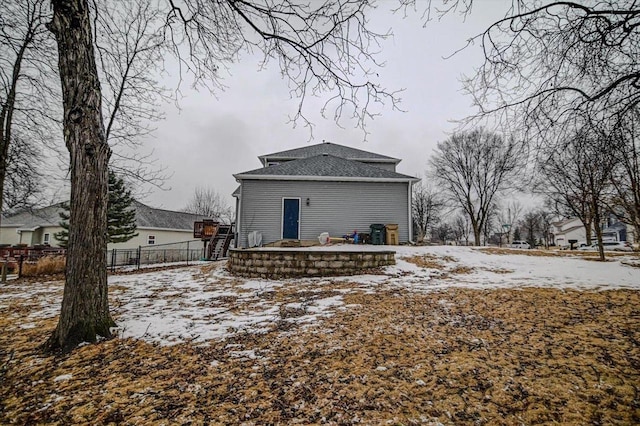 snow covered house featuring a shingled roof and fence