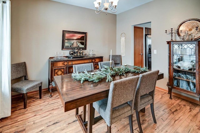 dining room featuring light wood finished floors, a notable chandelier, and baseboards