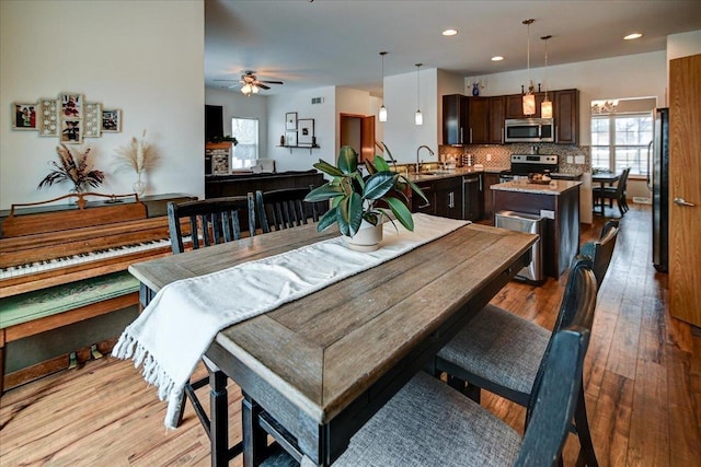 dining room featuring a ceiling fan, a stone fireplace, recessed lighting, and light wood finished floors