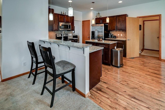 kitchen with a peninsula, dark brown cabinets, appliances with stainless steel finishes, and light wood finished floors