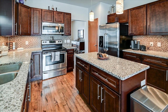 kitchen featuring light wood finished floors, backsplash, a center island, decorative light fixtures, and stainless steel appliances