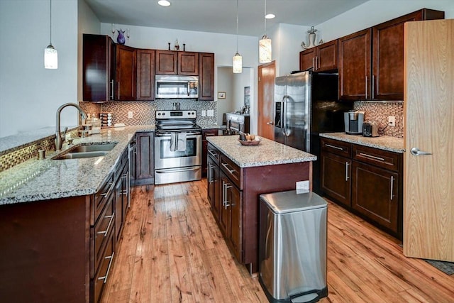 kitchen with light wood finished floors, appliances with stainless steel finishes, light stone counters, and a sink