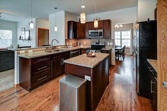 kitchen with decorative backsplash, appliances with stainless steel finishes, a peninsula, hardwood / wood-style flooring, and a sink