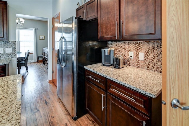 kitchen with light stone countertops, dark brown cabinetry, light wood-style floors, stainless steel fridge, and backsplash