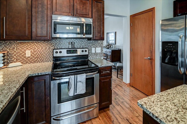 kitchen featuring decorative backsplash, appliances with stainless steel finishes, light wood-type flooring, and light stone countertops