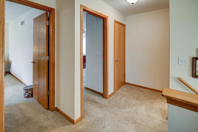 hall with visible vents, baseboards, and light colored carpet