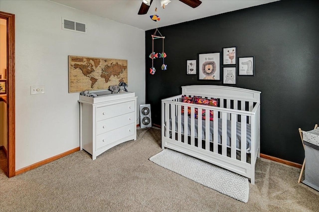 bedroom featuring carpet, visible vents, baseboards, ceiling fan, and a crib