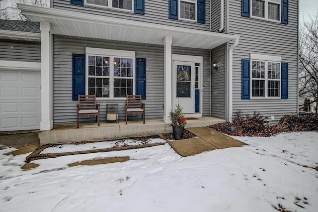 snow covered property entrance featuring an attached garage and covered porch