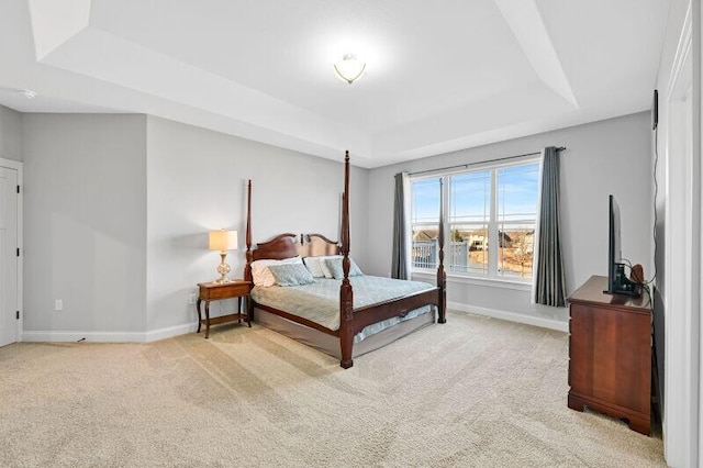 bedroom with a tray ceiling, light colored carpet, and baseboards