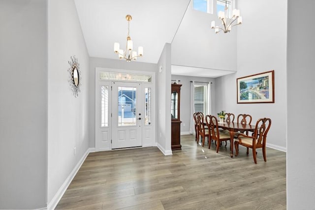 entryway with a chandelier, a towering ceiling, baseboards, and wood finished floors