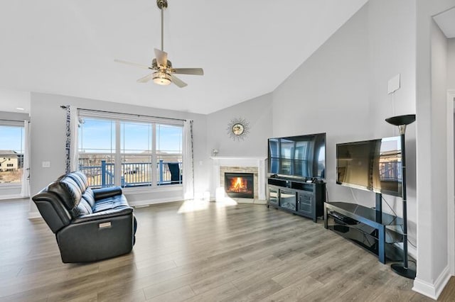 living area featuring baseboards, high vaulted ceiling, a stone fireplace, and wood finished floors