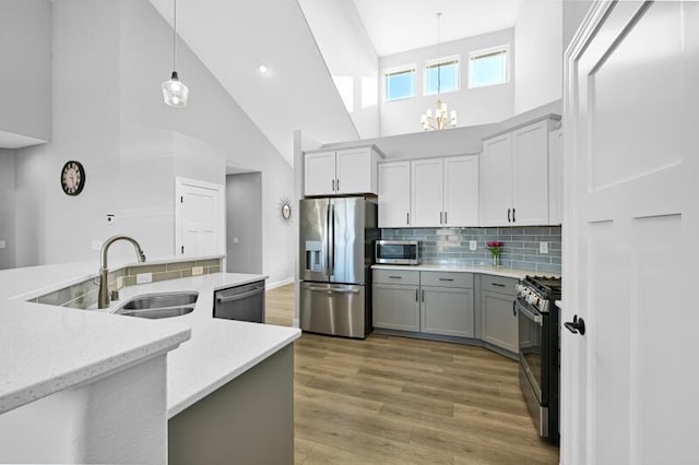 kitchen featuring backsplash, appliances with stainless steel finishes, light wood-style floors, hanging light fixtures, and a sink