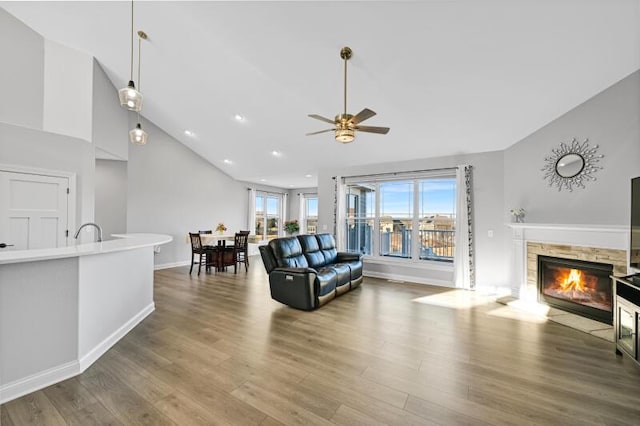 living room featuring a fireplace with flush hearth, high vaulted ceiling, wood finished floors, recessed lighting, and baseboards