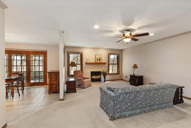 living room featuring a ceiling fan, baseboards, a fireplace with flush hearth, ornamental molding, and light carpet