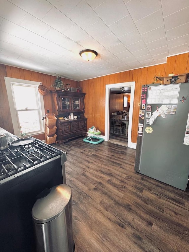 kitchen with wooden walls, dark wood finished floors, gas range, brown cabinets, and freestanding refrigerator