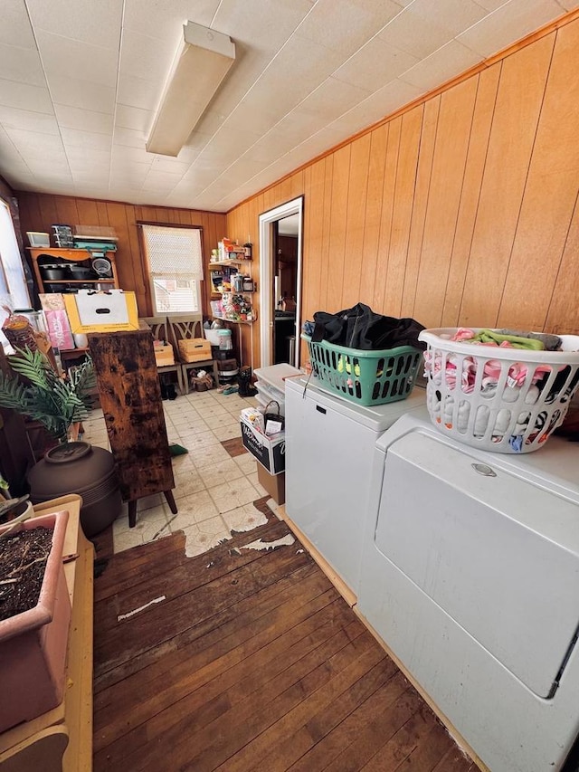 laundry room featuring wood-type flooring, wooden walls, and washing machine and clothes dryer