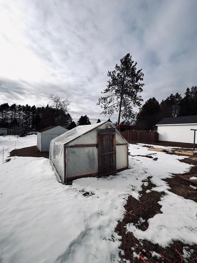 snow covered structure featuring a greenhouse, an outbuilding, and fence