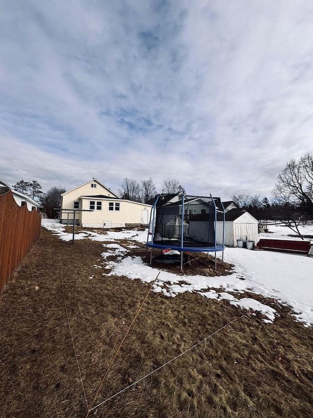 yard covered in snow featuring a trampoline and fence