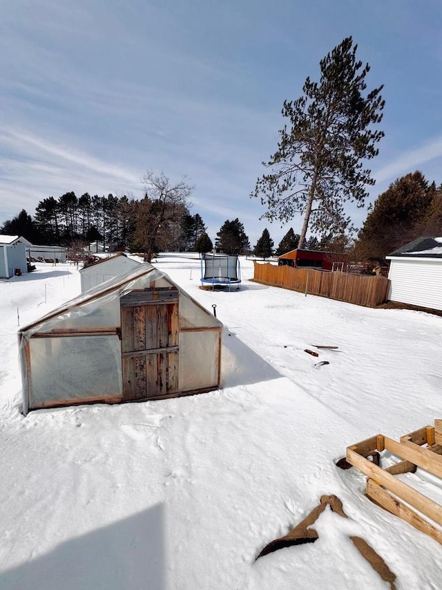 snowy yard with a trampoline, an outdoor structure, and fence