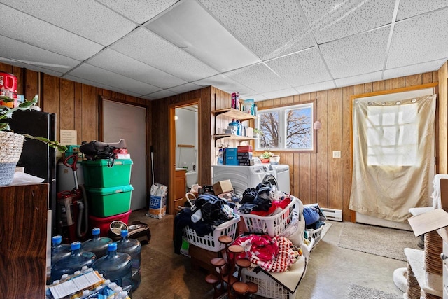 below grade area featuring wooden walls, independent washer and dryer, a baseboard radiator, and a drop ceiling