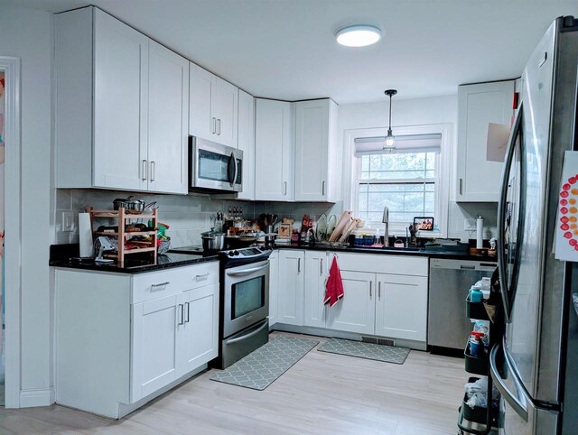 kitchen with a sink, stainless steel appliances, white cabinets, dark countertops, and tasteful backsplash