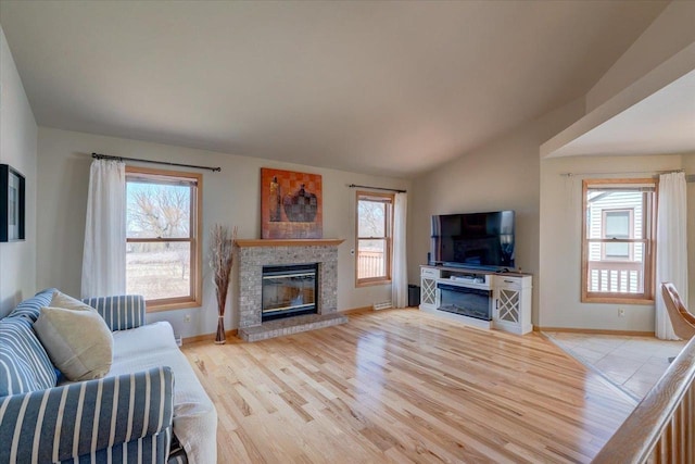 living area featuring wood finished floors, plenty of natural light, a glass covered fireplace, and vaulted ceiling