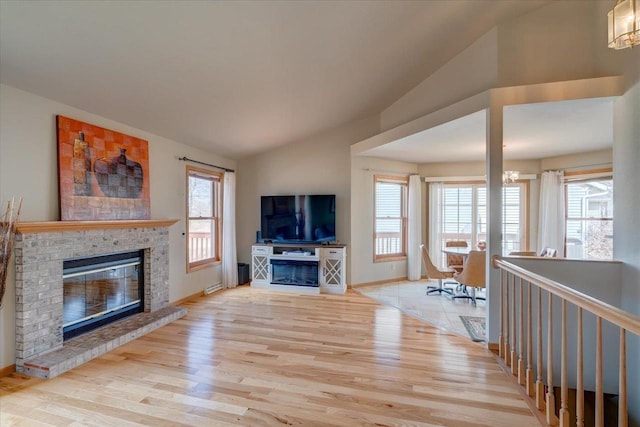 unfurnished living room featuring wood finished floors, baseboards, lofted ceiling, a brick fireplace, and a chandelier