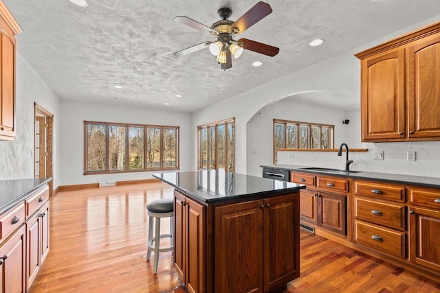 kitchen featuring a breakfast bar area, arched walkways, a sink, light wood-type flooring, and a center island