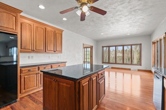 kitchen featuring light wood-type flooring, black refrigerator, a textured ceiling, brown cabinets, and a center island