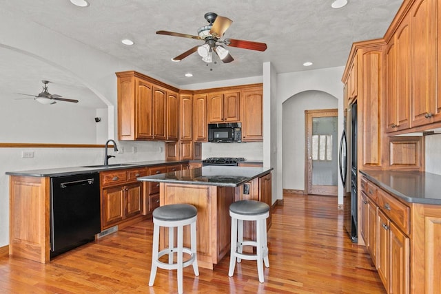 kitchen with a kitchen bar, black appliances, a sink, a kitchen island, and arched walkways