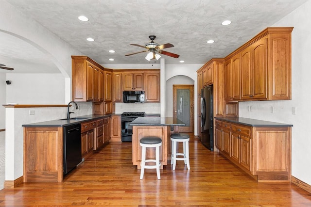 kitchen with black appliances, a sink, a kitchen breakfast bar, dark countertops, and ceiling fan