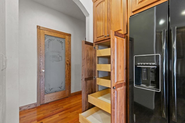 kitchen featuring light wood-style flooring, black fridge with ice dispenser, arched walkways, and baseboards