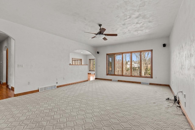 unfurnished living room featuring ceiling fan, visible vents, arched walkways, and baseboards