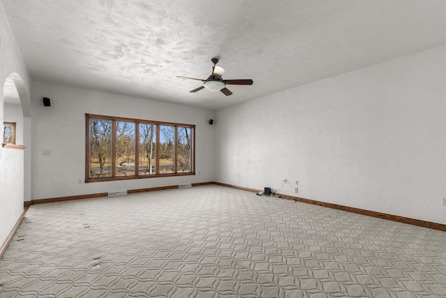 unfurnished room with visible vents, a textured ceiling, arched walkways, baseboards, and ceiling fan