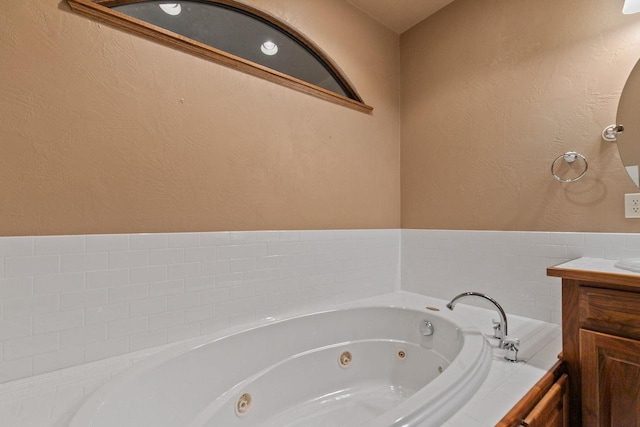 full bath featuring a whirlpool tub, vanity, and a textured wall