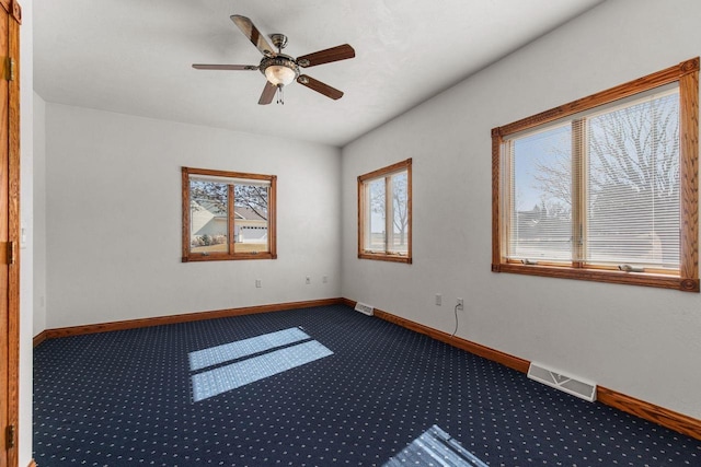 unfurnished room with visible vents, dark carpet, a ceiling fan, and baseboards