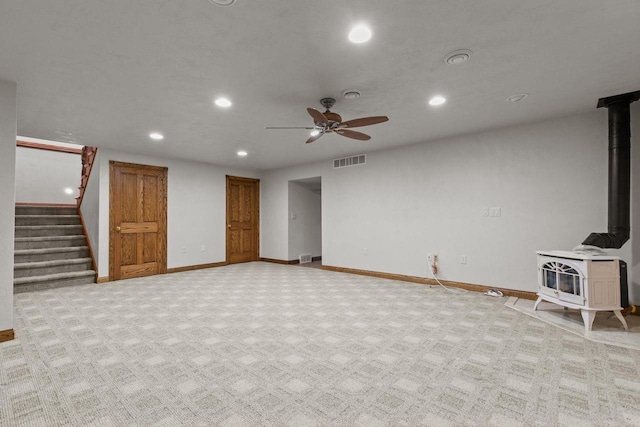 unfurnished living room with visible vents, a wood stove, baseboards, light colored carpet, and stairs