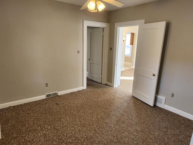 carpeted spare room with visible vents, baseboards, and ceiling fan