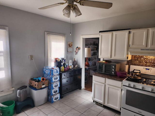 kitchen with under cabinet range hood, white cabinets, gas stove, and dark countertops