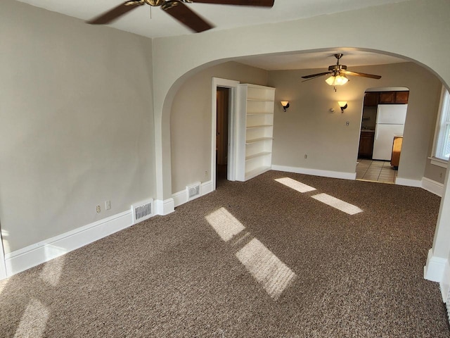 carpeted empty room featuring visible vents, arched walkways, baseboards, and ceiling fan