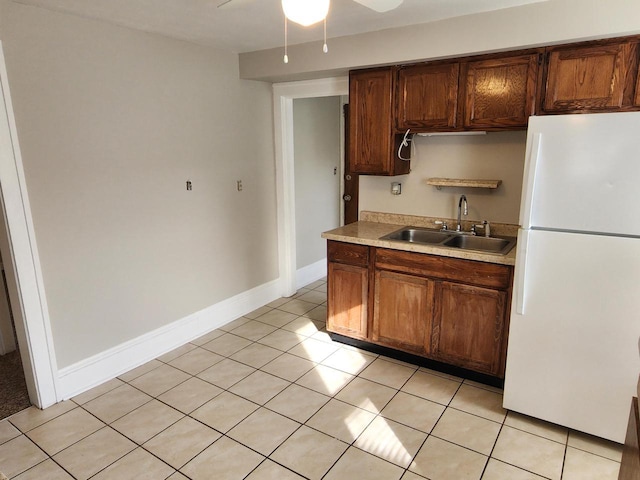 kitchen featuring a sink, freestanding refrigerator, light countertops, light tile patterned floors, and baseboards